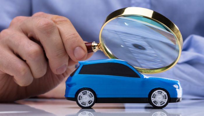 Close-up Of A Person's Hand Holding Magnifying Glass Over Small Blue Car